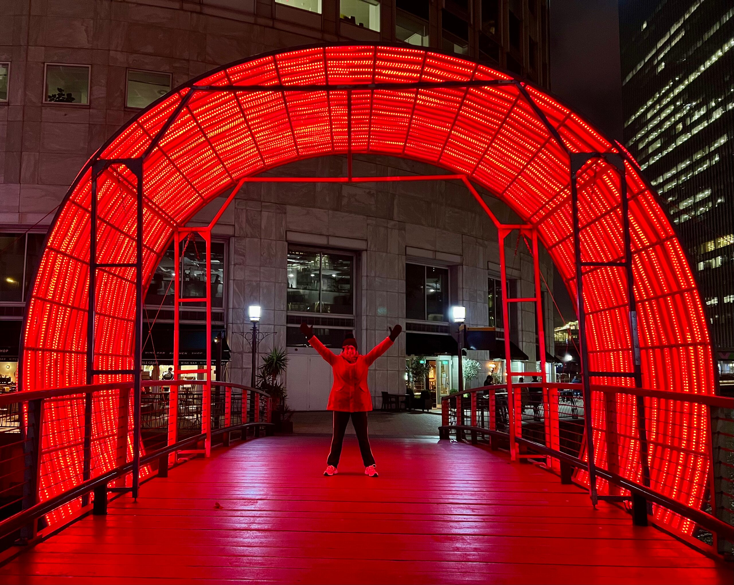 A person raising both arms beneath an illuminated red arch at night.