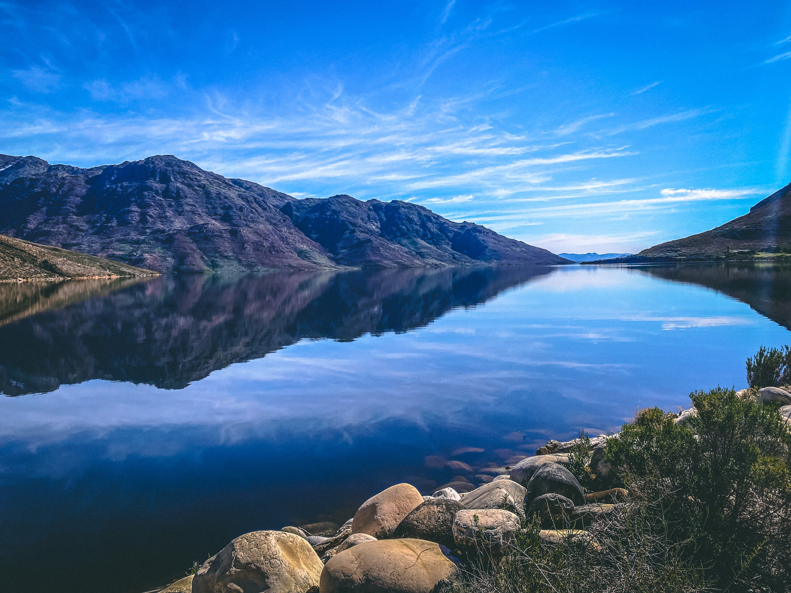 A mountain reservoir reflecting blue sky, ridges and clouds.
